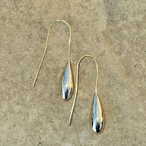 May include: A pair of gold teardrop earrings with a shiny finish. The earrings are simple and elegant.