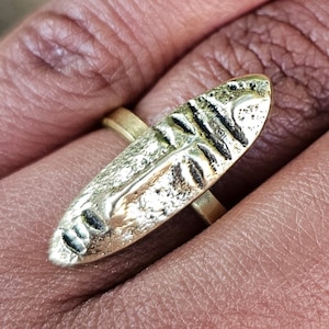 May include: A gold-toned ring with a textured, abstract design. The ring is worn on a finger.