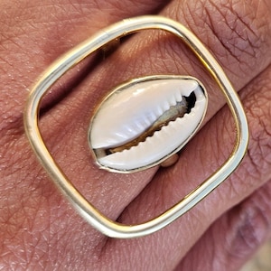May include: A gold ring with a square frame and a white seashell in the center.