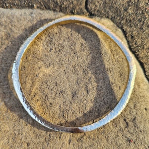 May include: A silver-colored, hammered metal bangle bracelet. The bracelet has a textured surface and a simple, elegant design. The bracelet is circular and appears to be made of a solid metal.