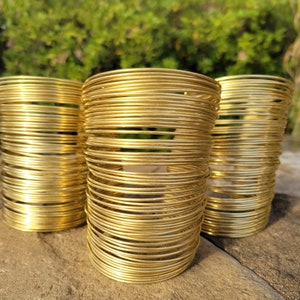 May include: Three gold-colored metal bangles stacked on top of each other. The bangles are made of thin, round wire that is tightly wound together.