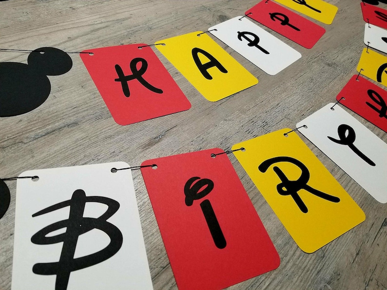 Puede incluir: Una pancarta en blanco y negro con las palabras "Happy Birthday" en letras negras sobre un fondo rojo, blanco y amarillo. La pancarta est&aacute; enhebrada con una cuerda negra.