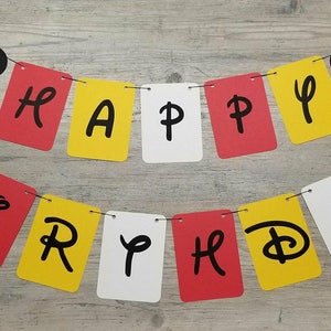Puede incluir: Una pancarta roja, amarilla y blanca con las palabras "Happy Birthday" en letras negras. La pancarta est&aacute; decorada con cabezas de Mickey Mouse negras.
