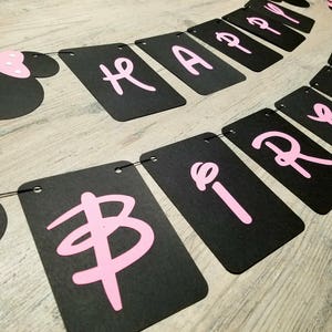 May include: Black and pink banner with the words "Happy Birthday" in pink letters. The banner is strung together with black string and has a black and pink Minnie Mouse head at the end.