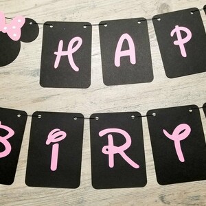 May include: Black and white banner with pink letters spelling "Happy Birthday". The banner has a Minnie Mouse head at the top with a pink bow.