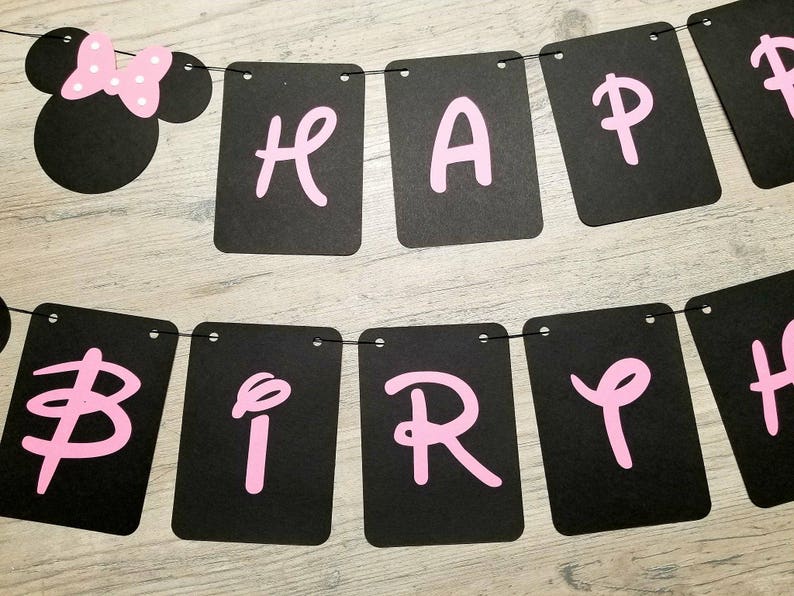 May include: Black and white banner with pink letters spelling "Happy Birthday". The banner has a Minnie Mouse head at the top with a pink bow.