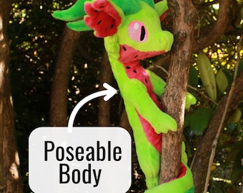 May include: A bright green plush dragon toy with pink accents on its ears, chest, and tail. The dragon has large pink eyes and a long, slender form. A white rectangular sign with a curved arrow points to the dragon, displaying the text Poseable Body.