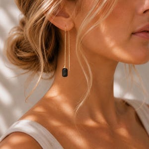 May include: A gold-toned threader earring featuring a delicate chain that passes through the earlobe. The earring is finished with a small, cylindrical, textured black bead dangling from the end of the chain, creating a minimalist drop design.
