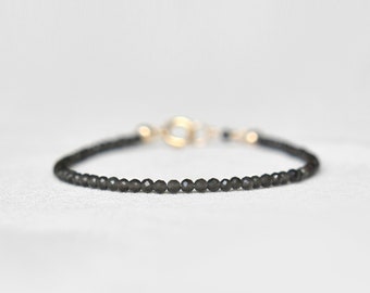 Peut inclure: Bracelet délicat composé de perles noires et d'un fermoir doré. Le bracelet est fait de petites perles rondes et sombres enfilées ensemble. Le fermoir est de conception simple et élégante. Sur fond blanc.