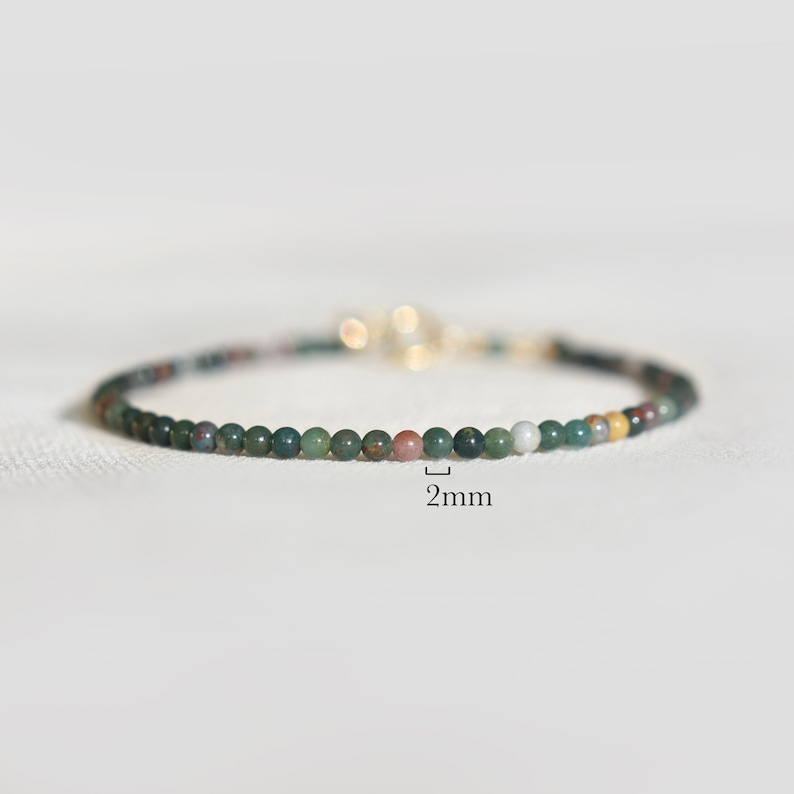 May include: A delicate beaded bracelet featuring small, round, multi-colored stones in shades of dark green, brown, and cream. The beads measure 2mm in diameter as indicated by the text label. A gold-toned metal clasp is visible at the back.