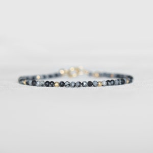 May include: A delicate bracelet made with black and grey gemstone beads and gold accents.