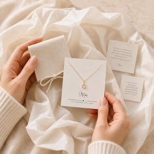 May include: A gold necklace with a teardrop-shaped pendant displayed on a white card featuring the text Olivia Mabrey, Handmade with heart in San Diego, and oliviamabrey.etsy.com, accompanied by a beige velvet pouch and two small note cards.