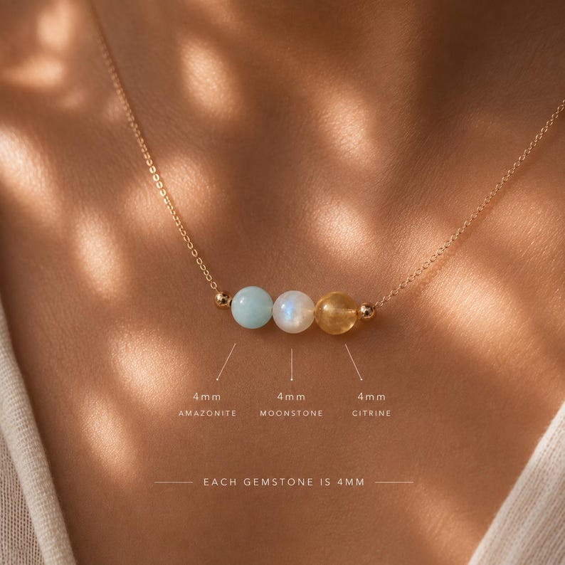 May include: A delicate gold chain necklace featuring three 4mm round gemstones: a light blue amazonite, a white moonstone, and a yellow citrine. The text labels indicate each gemstone is 4mm in size, with the total gemstone size being 4mm.