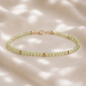May include: A delicate bracelet featuring a continuous strand of small, faceted light green beads interspersed with smooth, polished gold-toned metal spheres. The piece is finished with a simple gold-toned metal clasp mechanism at the centre.