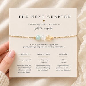 May include: A delicate gold chain bracelet featuring three small round gemstones: a light blue amazonite, a clear moonstone, and a yellow citrine. The bracelet is displayed on a cream-colored card with the text THE NEXT CHAPTER and descriptions of the stones.