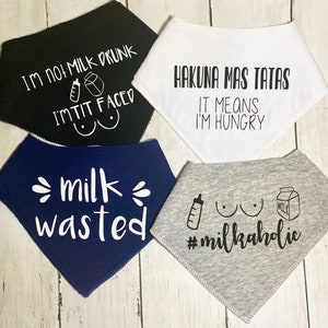 May include: Four baby bibs with humorous sayings about milk. The bibs are in black, white, blue, and gray. The sayings are "I'm not milk drunk I'm tit faced", "Hakuna Mas Tatas It means I'm hungry", "Milk wasted", and "#milkaholic".