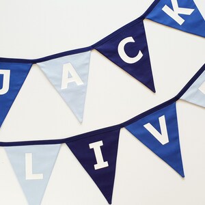 May include: A blue and white pennant banner with the names "JACK" and "OLIVER" spelled out in white capital letters. The pennants are in shades of blue, with a white background.