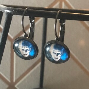 May include: A pair of silver hoop earrings with a blue and white image of a face on each earring.
