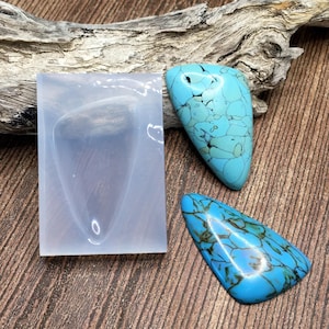 May include: A clear silicone mold for making jewelry with a triangular shape. Two turquoise cabochons are shown next to the mold.