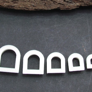 May include: Five white plastic arch-shaped cookie cutters of varying sizes. The cutters are arranged in a row from largest to smallest.
