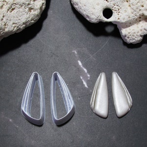 Può includere: Due paia di orecchini d'argento. Un paio ha una forma semplice e curva, l'altro ha una forma più geometrica e angolare.