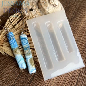 May include: Earrings with a blue, white, and gold swirl pattern. The earrings are hanging next to a silicone mold with three rectangular cavities. The text "Jessama Design" is visible in the upper left corner.