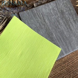 May include: Two textured, square tiles. One is a bright lime green, the other is a dark gray. Both have a linear, wood-grain-like texture. The tiles are angled, with the green tile in the foreground and the gray tile in the background.
