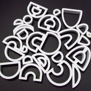 May include: A collection of white plastic cookie cutters in various shapes, including circles, semicircles, and arches.