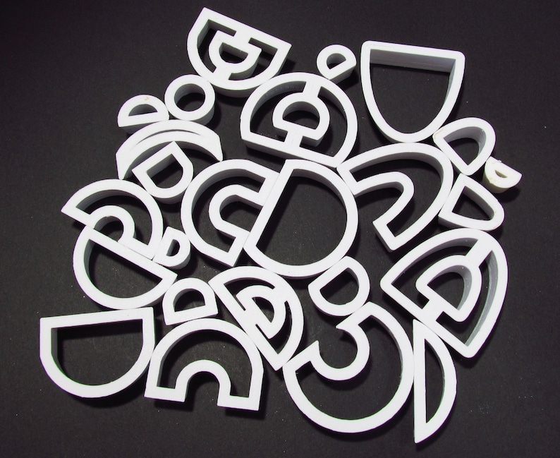 May include: A collection of white plastic cookie cutters in various shapes, including circles, semicircles, and arches.