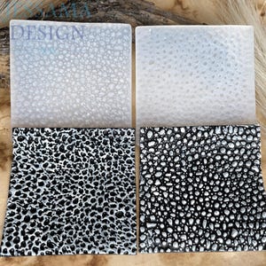 Può includere: Quattro sottobicchieri quadrati con superfici strutturate. Due sono bianchi, uno è nero e uno è bianco e nero. La parola "DESIGN" è visibile nell'angolo in alto a sinistra.