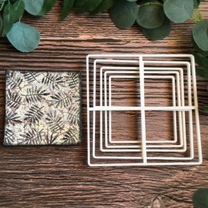 May include: A white ceramic square cake stand with a decorative leaf pattern. The stand is made of multiple layers and is perfect for displaying cakes, pastries, or other desserts.