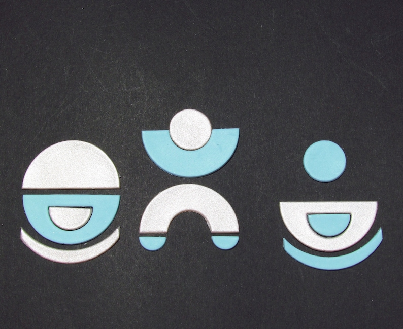 May include: Three abstract shapes made of white and light blue paper. The shapes are arranged in a row on a black background. The shapes are simple and geometric.