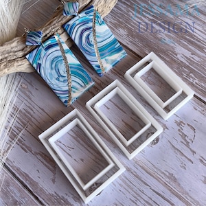 May include: Two rectangular earrings featuring a blue, white, and purple marbled pattern with a diagonal gold glitter stripe, paired with three sets of white plastic rectangular cookie cutters. The text JESSAMA DESIGN is visible.