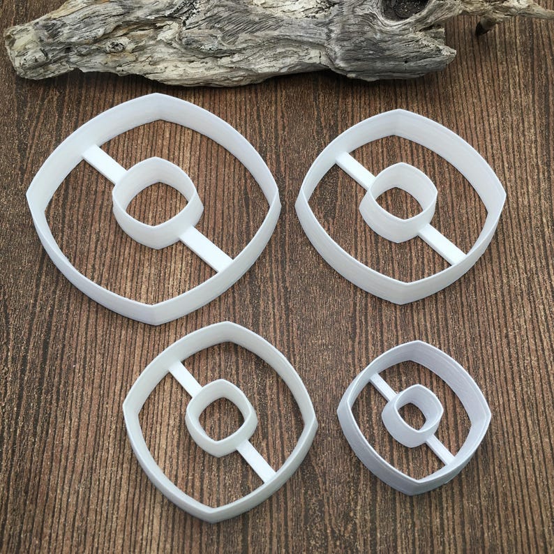 以下が含まれることがあります： 中央に線が引かれたドーナツの形をした白いプラスチック製のクッキーカッターが4つ。カッターはサイズが異なります。