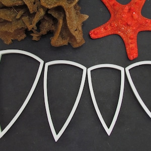 May include: Four white plastic cookie cutters shaped like triangles, on a black background.