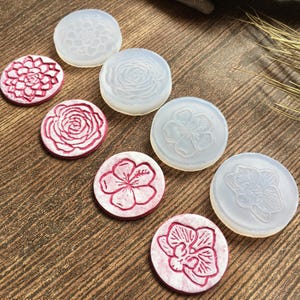 May include: A collection of round, floral-themed items. Some are white and translucent, while others are white with red floral designs. The items are arranged on a wooden surface, showcasing various flower patterns.