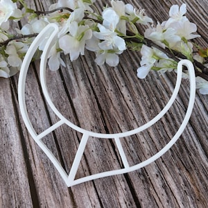 Op de afbeelding: Witte plastic koekjesvormer in de vorm van een halve maan met een geometrisch ontwerp. De vormer ligt op een houten oppervlak.