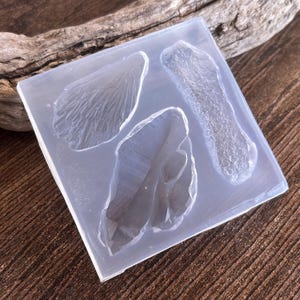 May include: A clear silicone mold with four different shapes: a leaf, a flower petal, and two irregular shapes. The mold is designed for creating resin crafts.