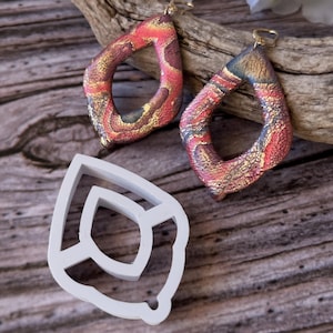May include: A pair of handmade polymer clay earrings with a red, gold, and brown marbled pattern. The earrings are shaped like teardrops with a hole at the top for a hook.