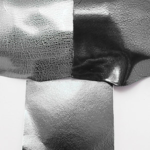 May include: Close-up of three samples of silver-colored faux leather. The leather has a textured, cracked surface.