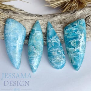 May include: Four blue and white resin nail art pieces in various shapes. The pieces have a marbled appearance with swirls of white and light blue. The pieces are arranged on a piece of driftwood.