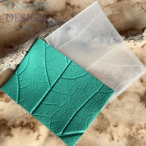 May include: A rectangular silicone mold featuring a detailed leaf vein pattern, shown alongside a green textured impression of the same leaf design. The mold is translucent and flexible, displaying a clear network of veins across its surface.
