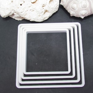 May include: Four white plastic square cookie cutters of different sizes, stacked on top of each other.
