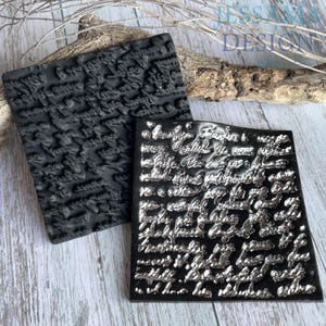 May include: Two square rubber stamps featuring raised, intricate cursive handwriting text. One stamp is solid matte black, while the other has a metallic silver finish on the raised lettering, creating a high-contrast effect for detailed printing.
