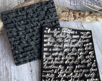 May include: Two square rubber stamps featuring raised, intricate cursive handwriting text. One stamp is solid matte black, while the other has a metallic silver finish on the raised lettering, creating a high-contrast effect for detailed printing.
