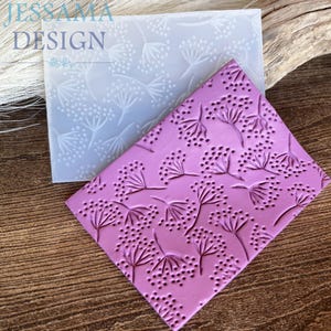May include: A pink, diamond-shaped embossing mould with a floral pattern, next to a clear mould with the same design. The moulds feature a repeating pattern of stylized flowers and the text "JESSAMA DESIGN".