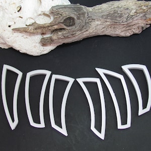 May include: Seven white plastic cookie cutters shaped like curved, pointed leaves. The cutters are arranged in a semi-circle on a black surface.