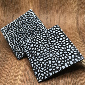May include: Two square black coasters with a raised white pebble pattern.