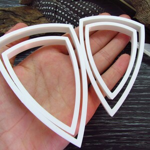 May include: Three white plastic triangle-shaped cookie cutters of different sizes.