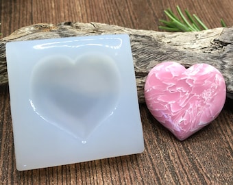May include: A clear silicone mold shaped like a heart, next to a pink heart-shaped resin piece with a marbled pattern.